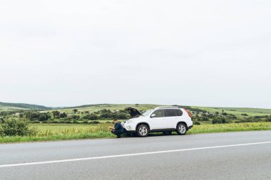 kırık arabanın yakınında telefon ile oturan adam yardım arıyor. Road trip sorunları