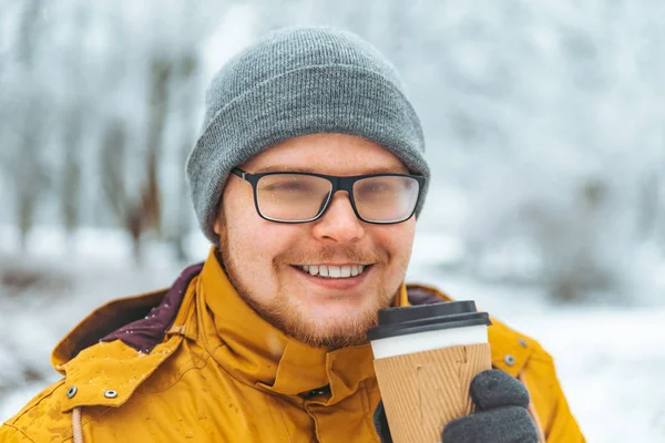 man drinking coffee to go outside in snowed winter day. glasses is misted. close up portrait