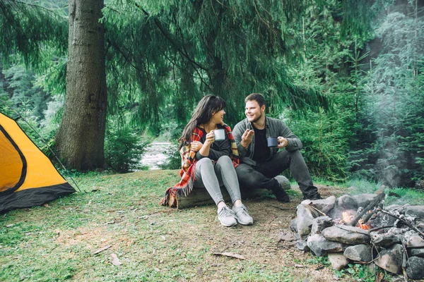 couple sitting near camp fire and drinking tea and telling stories . tent and suv on background. union with nature