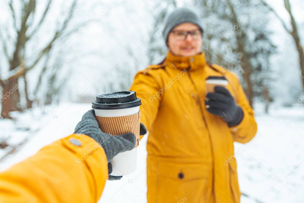 man bring coffee to go for friends in snowed city park. winter season