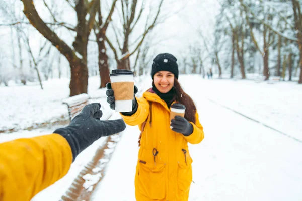 woman give cup of coffee to friend. meeting in snowed winter park concept