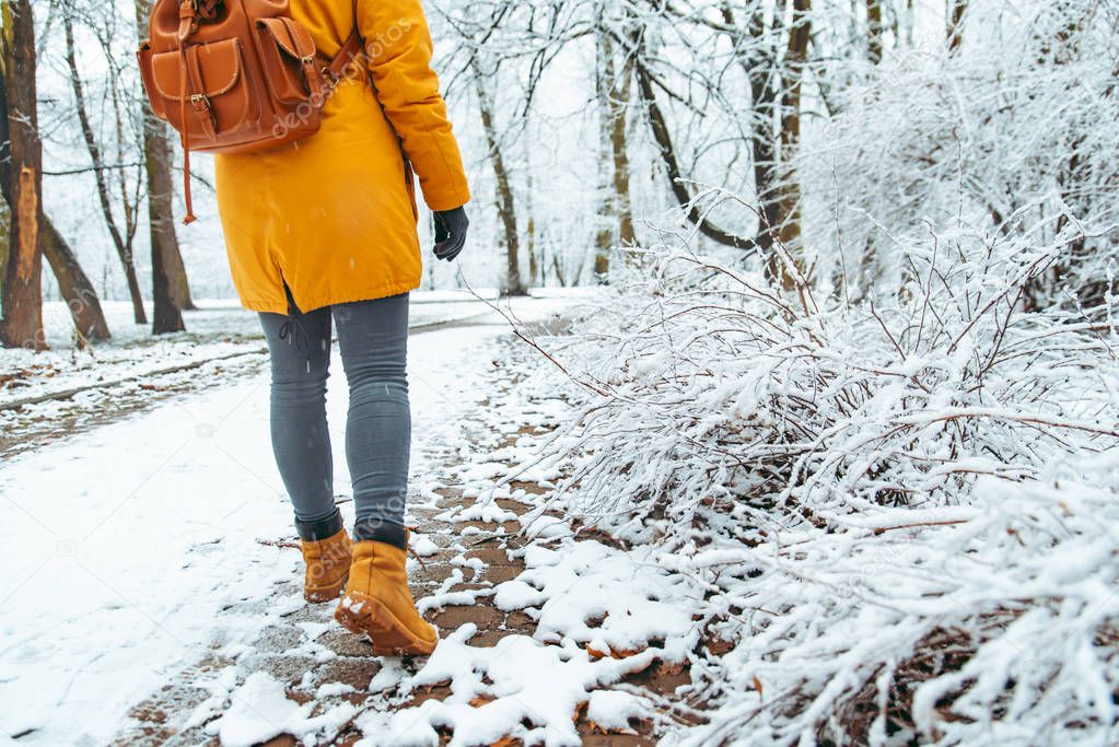 woman walking by snowed city park. view from behind. backpack. winter concept