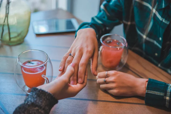 woman shows engagement ring to friend in cafe while drinking warm up fruit tea