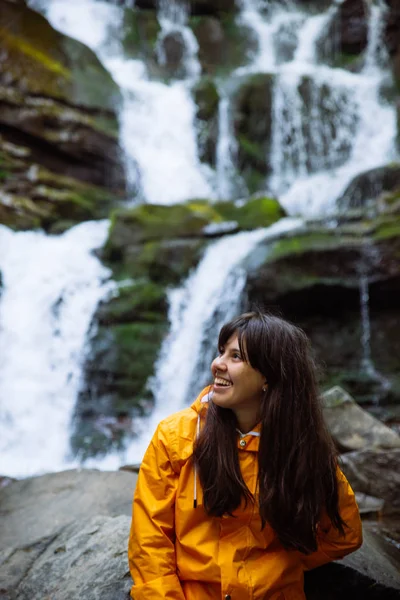 Donna sorridente in impermeabile giallo con cascata sullo sfondo — Foto Stock