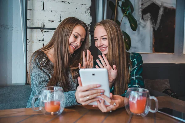 Two young beauty women talking by video chat using tablet. sitting in cafe drinking tea — Stock Photo, Image