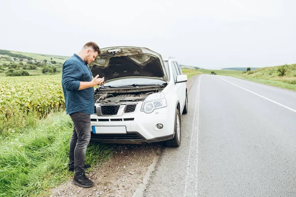 man stand in front of broken car with phone. broken in the middle of nowhere