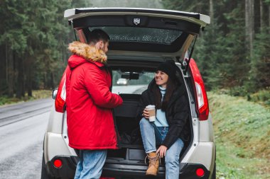 Çift sıcak çay içmeyi kes. yol gezi konsepti. suv gövde dağlar ormandaki yol tarafında oturan. hayat tarzları