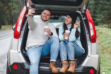 Erkek ve kadın sıcak çay ve alma selfie araba suv gövde içmeyi kes. yol gezi konsepti