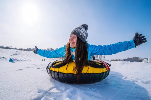 young pretty woman at snow tubing rise hands up. slide from snow hill. winter activity