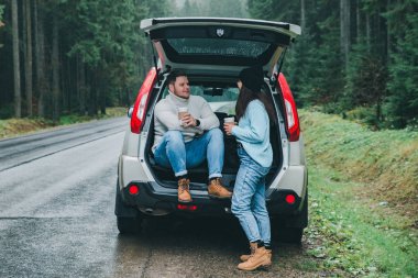 Çift sıcak çay içmeyi kes. yol gezi konsepti. suv gövde dağlar ormandaki yol tarafında oturan. hayat tarzları