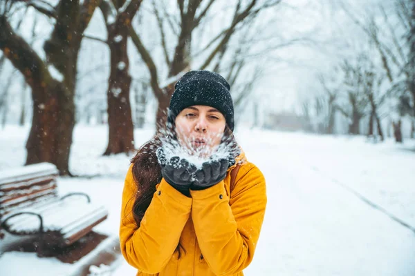 女性は彼女の手から吹雪します 背景に雪が降った公園 冬シーズン コンセプト — ストック写真