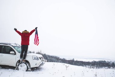 Tepenin tepesinde elinde ABD bayrağı olan bir adam arazi aracının yanında güzel bir kış manzarası arıyor. özgürlük kavramı