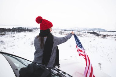 ABD bayrağı ile Cipin kaputunun üzerinde oturan genç yetişkin kadın gezgin. araba seyahat