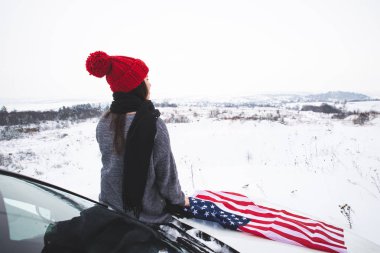 ABD bayrağı ile Cipin kaputunun üzerinde oturan genç yetişkin kadın gezgin. araba seyahat
