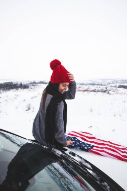 ABD bayrağı ile Cipin kaputunun üzerinde oturan genç yetişkin kadın gezgin. araba seyahat