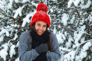 Arka planda bubo köknar ağacı olan kırmızı şapkalı, kışın gülümseyen genç kadın portresi. şık konsept
