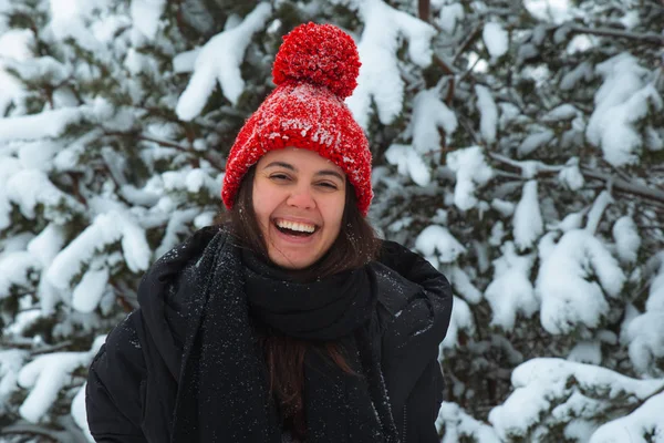 Arka planda bubo köknar ağacı olan kırmızı şapkalı, kışın gülümseyen genç kadın portresi. şık konsept