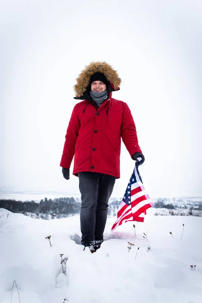 Man in red winter coat holding usa flag outdoors in snowy weather — Stock Photo, Image