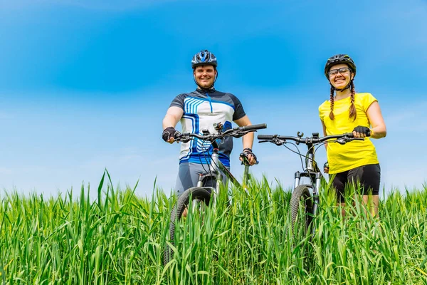 若い強者と自転車で緑の草原に立っている女性の笑顔します ライフ スタイル — ストック写真