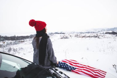 ABD bayrağı ile Cipin kaputunun üzerinde oturan genç yetişkin kadın gezgin. araba seyahat