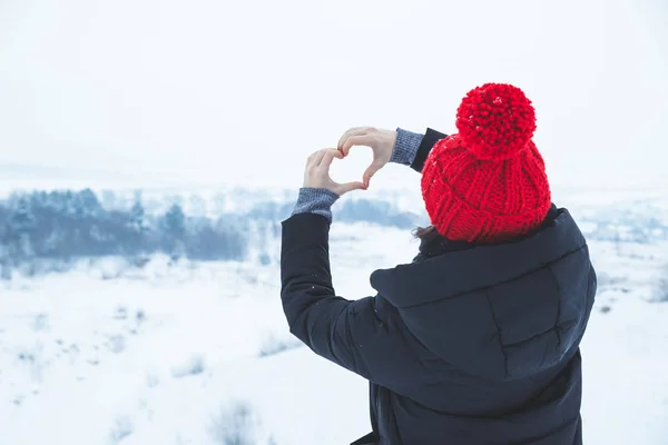 woman in red hat make love symbol with her hands. winter time. snowfall