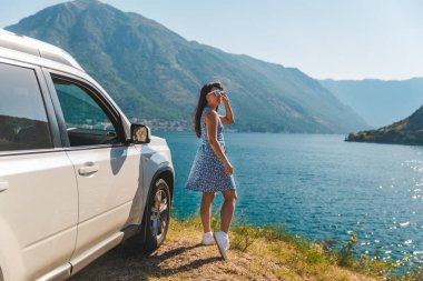 cliff yakınındaki beyaz jip araba güzel dağlar ile defne deniz manzarasına sahip üzerinde duran kadın. araba yolculuğu