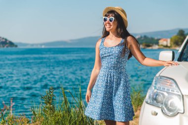 mavi elbise ayakta beyaz car, defne ve dağların güzel manzaralı sahil yakınındaki kadında. yaz seyahat kavramı