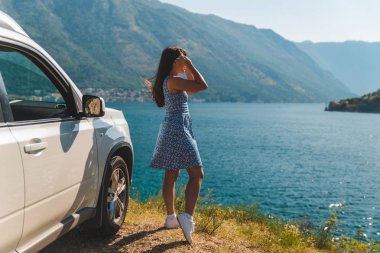 cliff yakınındaki beyaz jip araba güzel dağlar ile defne deniz manzarasına sahip üzerinde duran kadın. araba yolculuğu