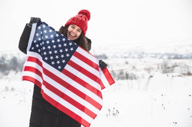 kırmızı şapkalı ABD bayrağı tutan genç gülümseyen kadın. kış zamanı. vatansever kavramı