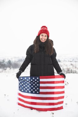 kırmızı şapkalı ABD bayrağı tutan genç gülümseyen kadın. kış zamanı. vatansever kavramı