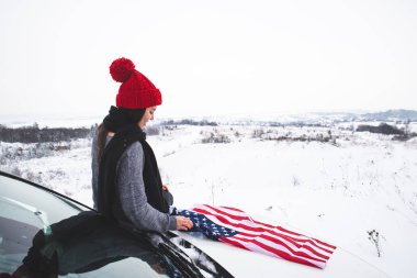 ABD bayrağı ile Cipin kaputunun üzerinde oturan genç yetişkin kadın gezgin. araba seyahat
