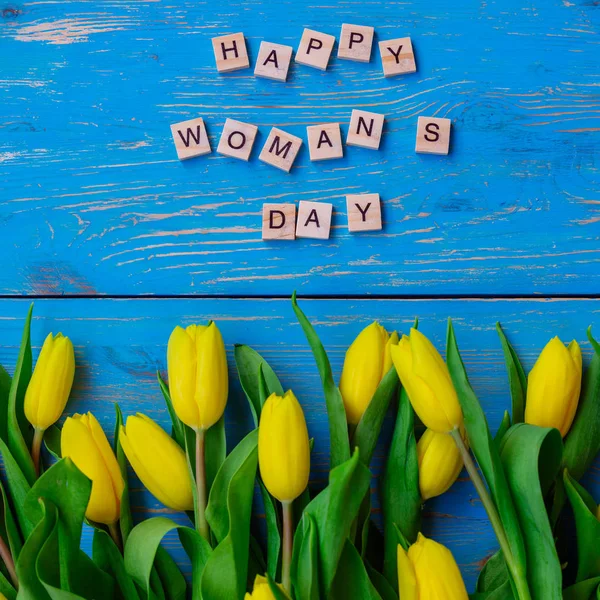 happy woman\'s day text. tulips overhead on blue wooden background