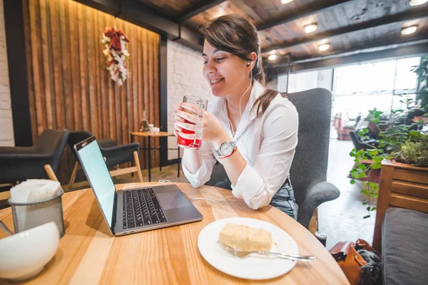食べたり飲んだり ヘッドセットで音楽を聴くのラップトップでカフェに座っている作業負荷の高いきれいな女性 ライフ スタイルのコンセプト フリーランス — ストック写真