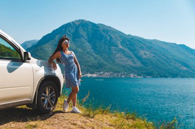 cliff yakınındaki beyaz jip araba güzel dağlar ile defne deniz manzarasına sahip üzerinde duran kadın. araba yolculuğu