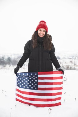 kırmızı şapkalı ABD bayrağı tutan genç gülümseyen kadın. kış zamanı. vatansever kavramı