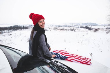 ABD bayrağı ile Cipin kaputunun üzerinde oturan genç yetişkin kadın gezgin. araba seyahat