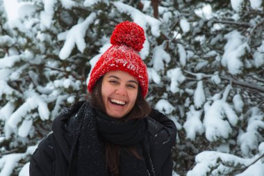 Arka planda bubo köknar ağacı olan kırmızı şapkalı, kışın gülümseyen genç kadın portresi. şık konsept