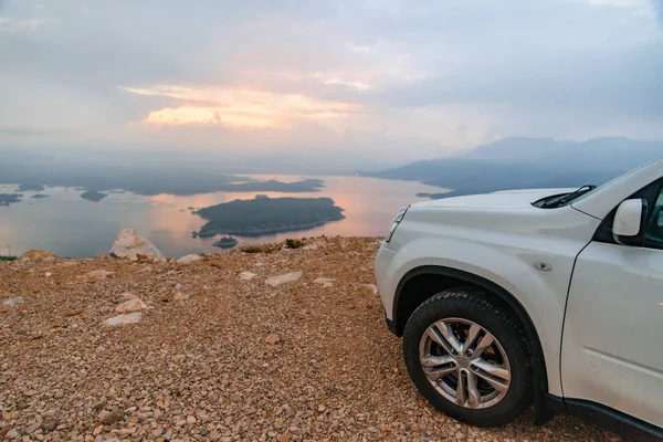white suv car at cliff sunrise over lake on background. road trip