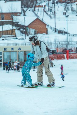 LVIV, UKRAINE - 12 Ocak 2019: Anne küçük kıza snowboard öğretiyor. Yaşam tarzı. kış aktiviteleri