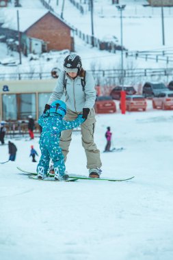 LVIV, UKRAINE - 12 Ocak 2019: Anne küçük kıza snowboard öğretiyor. Yaşam tarzı. kış aktiviteleri
