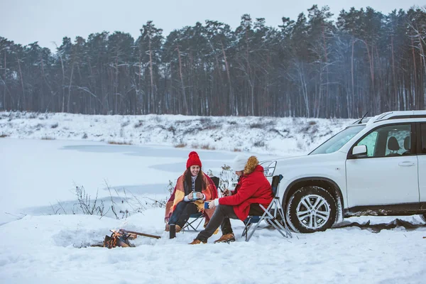 man with woman sitting on chairs near camp fire in winter time. car travel. active lifestyle