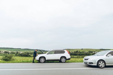 adam ayakta kırık araba ile açılan kukuleta yakınındaki. Acil servis. başarısız bir yolculuk