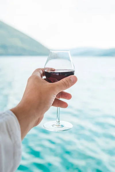 男の手は海と山を背景に赤ワインのガラスを保持しています ライフ スタイル — ストック写真