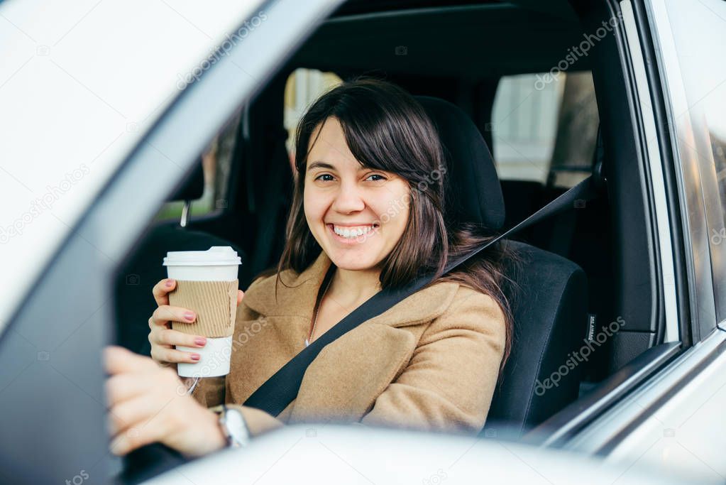 young smiling woman driving car. safety belt. drinking coffee