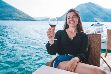 gülümseyen genç kadın, güzel dağ manzaralı sahil kırmızı şarap içme. kafede dinlenme
