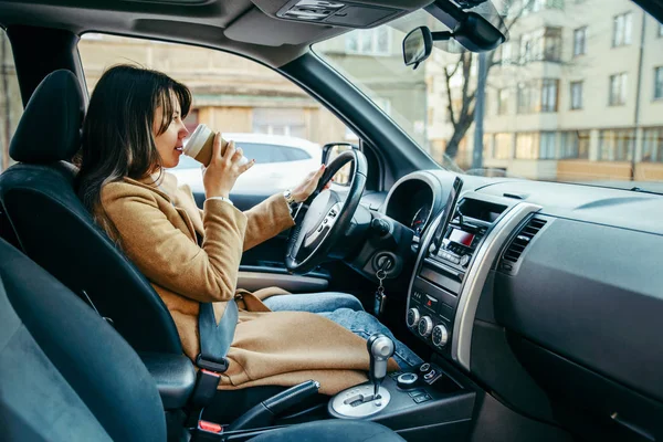 Mladá krásná žena, která řídila auto při pití šálku kávy — Stock fotografie