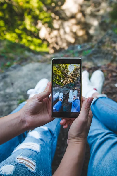 Casal sentado no chão tirando fotos de pernas no telefone — Fotografia de Stock