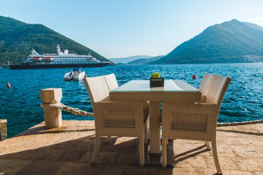güzel bir deniz ve dağ manzarası ile sahilde Cafe tablo. üzerinde ayrılmış plaka. Cruise liner arka plan üzerinde