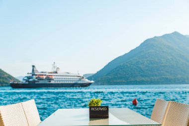 güzel bir deniz ve dağ manzarası ile sahilde Cafe tablo. üzerinde ayrılmış plaka. Cruise liner arka plan üzerinde
