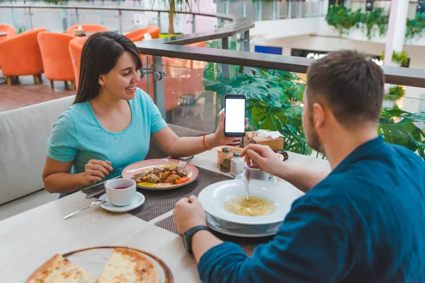दोन कॅफेमध्ये खातात. महिला फोन स्क्रीन दाखवते. पांढरा प्रत जागा — स्टॉक फोटो, इमेज